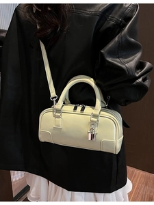 Chic cream square crossbody bag with silver lock and adjustable strap on a leather jacket