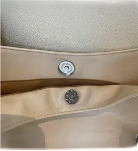 Détail des fermoirs magnétiques d'un sac bandoulière beige à texture de litchi