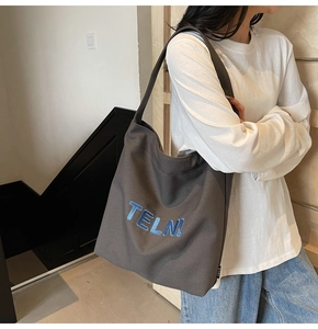 Dettaglio della grande borsa tote in tela con ricamo blu testurizzato su tessuto grigio scuro