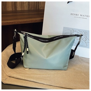 Detail of light green nylon crossbody bag showing the branded black strap and woven cord