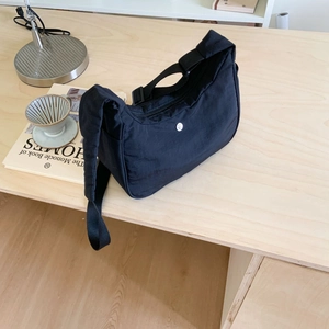 Sac croissant en nylon noir minimaliste avec bandoulière posé sur une table en bois
