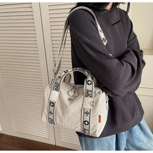 Dettaglio della borsa a tracolla in nylon beige con etichetta arancione e tracolla a motivi