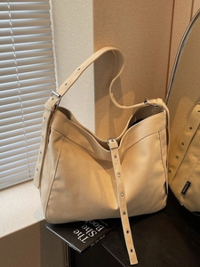 Minimalist cream canvas shoulder tote bag with adjustable metal eyelet strap in a soft room