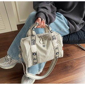 Dettaglio borsa a cilindro beige con tracolla ricamata e doppia chiusura a zip