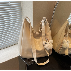 Détail du sac à bandoulière minimaliste blanc cassé avec breloque ours et sangle large