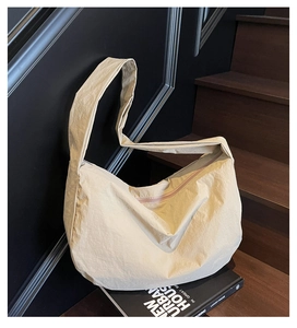Détail du sac bandoulière en nylon beige à texture plissée posé sur un livre contre un mur