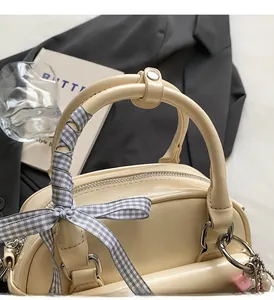 Détail d'un sac bowling crème avec poignées rondes et ruban décoratif à carreaux gris