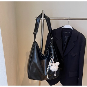 Gros plan d'un sac hobo noir avec un charme en peluche blanc suspendu à un support métal