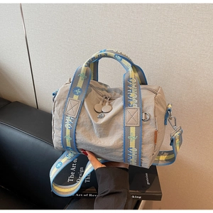 Dettaglio borsa a tracolla in nylon grigio con manici in tessuto colorato su divano