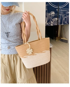 Detail of two-tone woven tote bag with wavy patterns and a decorative floral charm