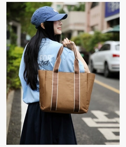 Outdoor street shot of a large brown canvas tote bag with striped straps for women