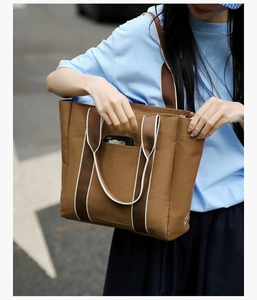 Detailed shot of large brown canvas tote bag with striped straps and front pocket