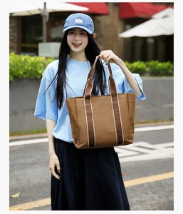 Close-up of a large brown canvas tote bag featuring stylish striped fabric handles