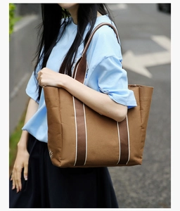 Detail of brown canvas tote bag with striped straps and sun embroidery on model