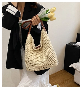 Detail of hand-woven straw tote bag with brown leather strap and minimalist design