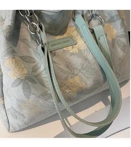 Detail of light green floral tote bag strap featuring silver metal chain and SAKURA logo