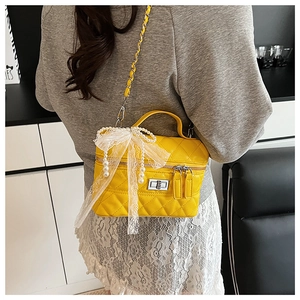 Détail d'un sac jaune à losanges avec nœud en dentelle et pampille de perles