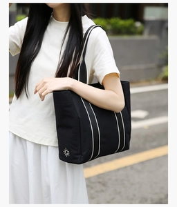 Model wearing a black canvas tote bag with white vertical stripes and sun embroidery detail