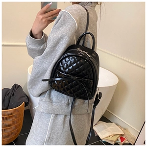 Détail d'un mini sac à dos noir matelassé avec nœud et finition brillante en cuir