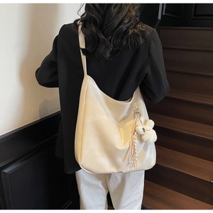 Vue détaillée d'un sac hobo blanc crème avec pendentif en peluche et pompon porté au dos
