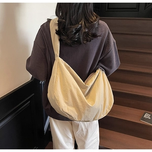 Détail d'un sac bandoulière en nylon crème avec large sangle sur un escalier en bois