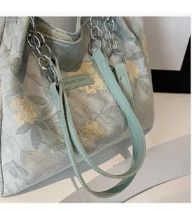 Detail of floral tote bag showing metal chain straps and SAKURA DIARY leather logo patch