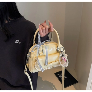 Detail of cream yellow bag featuring grey plaid bow, lace trim, and pearl charm