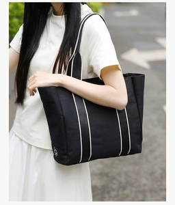 Detail of minimalist black canvas tote bag featuring embroidered sun logo and striped strap
