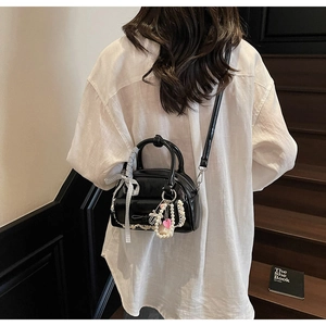 Détail du sac noir avec nœud et perles porté par un mannequin en chemise blanche