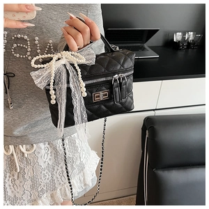 Détail du sac boîte en cuir matelassé noir avec nœud en dentelle perlée et chaîne