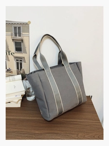 Detailed 45-degree angle view of a grey canvas tote bag with striped handles on a desk