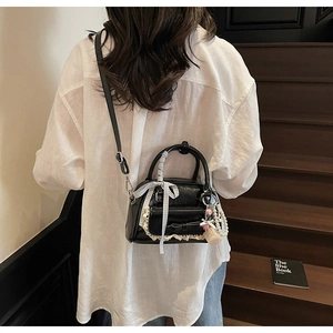 Glossy black mini bowling bag with lace trim and pearls shown on a model