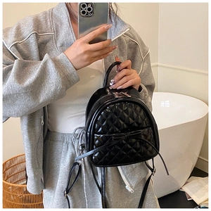 Détail d'un mini sac à dos noir matelassé en cuir brillant avec un nœud décoratif