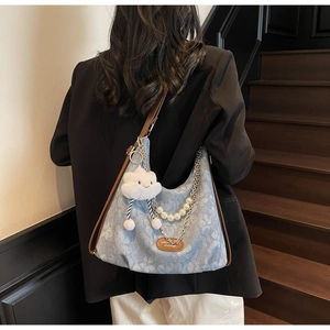 Détail du sac hobo en denim bleu avec motif floral, chaîne en perles et charme nuage peluche