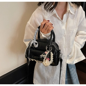 Détail du sac en cuir verni noir avec dentelle, ruban et pendentifs en perles