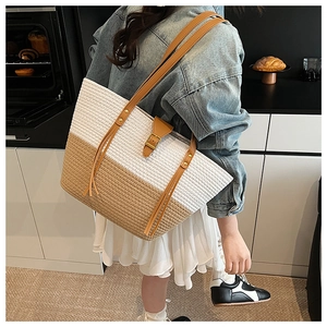 Dettaglio della borsa tote in paglia bicolore con manici in pelle marrone in casa