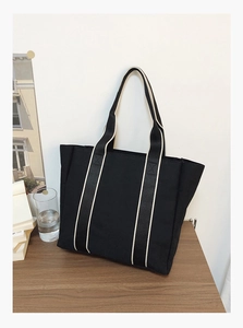 Detail of a large black canvas tote bag with contrast cream straps on a wooden table