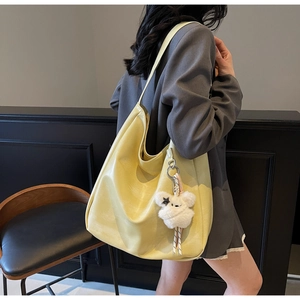 Détail d'un sac cabas jaune en PU sur l'épaule avec un pendentif ours en peluche