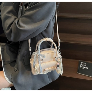 Detail of light beige bowling bag with lace trim, pearl pendant, and ribbon bows