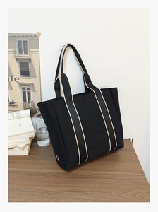 Detailed macro shot of black canvas tote bag featuring striped straps on wooden tabletop
