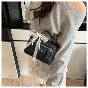 Détail du sac matelassé noir avec un grand nœud en dentelle blanche et perle élégante