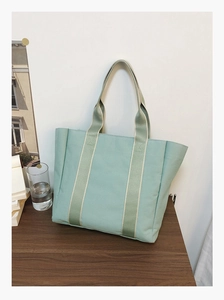 Close-up of mint green canvas tote bag with striped straps on a dark wood table