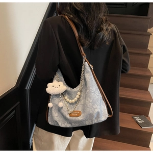 Blue floral canvas tote bag with pearl chain and cloud charm worn on a wooden staircase
