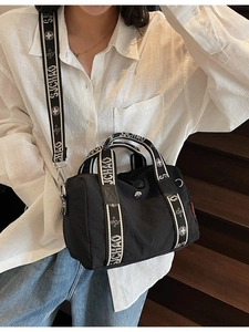 Borsa Boston nera in nylon con coulisse e tracolla in tessuto su scala di legno scuro