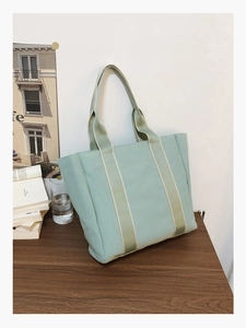 Close-up of a mint green canvas tote bag with striped straps on a wooden table