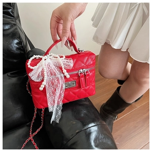 Détail du sac matelassé rouge avec nœud en dentelle blanche et fleurs en perles