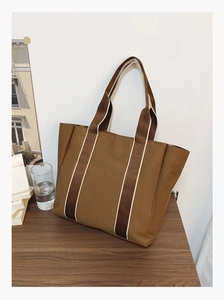 Detailed texture of brown canvas tote bag with striped fabric handles on a wooden table