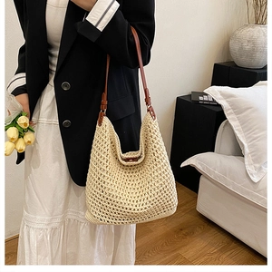 Detail of hand-woven straw bucket bag with brown leather strap on a lifestyle model