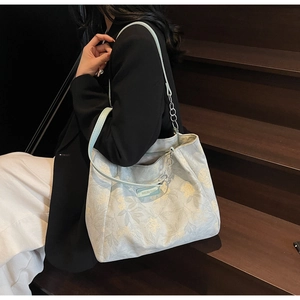 Light blue floral tote bag with green leather straps and silver chain detail on model
