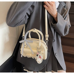 Close-up of cream bowling bag with ribbon, pearl charm, and delicate lace trim details